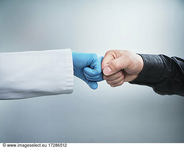 Weibliche Mitarbeiterin im Gesundheitswesen gibt einem männlichen Patienten einen Faustschlag vor weißem Hintergrund