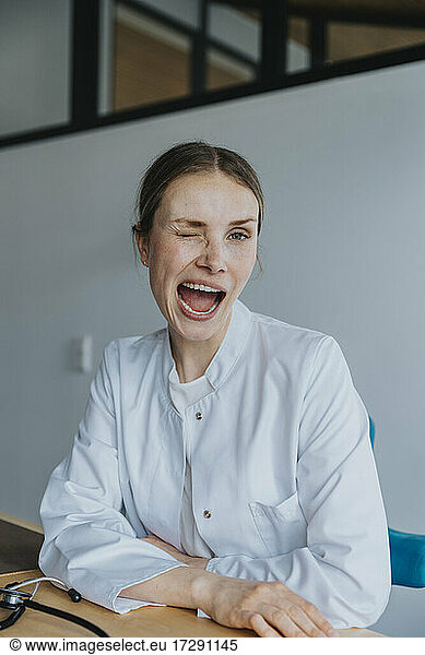Weibliche Mitarbeiterin im Gesundheitswesen mit offenem Mund  die am Schreibtisch ein Gesicht macht