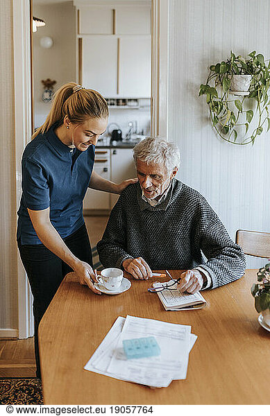 Weibliche Pflegehelferin serviert Tee für einen älteren Mann  der zu Hause sitzt