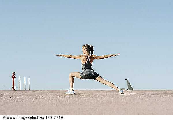Weibliche Sportlerin übt an einem sonnigen Tag die Position des Kriegers