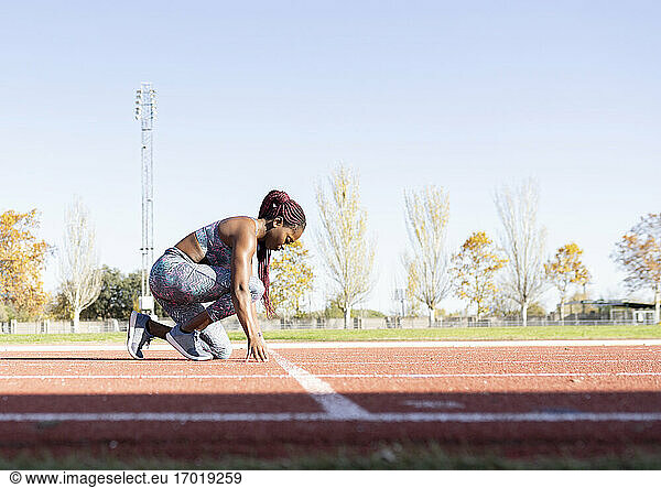 Weibliche Sportlerin in Startposition auf einer Sportbahn an einem sonnigen Tag