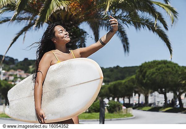 Weibliche Surferin mit Surfbrett macht ein Selfie mit ihrem Smartphone