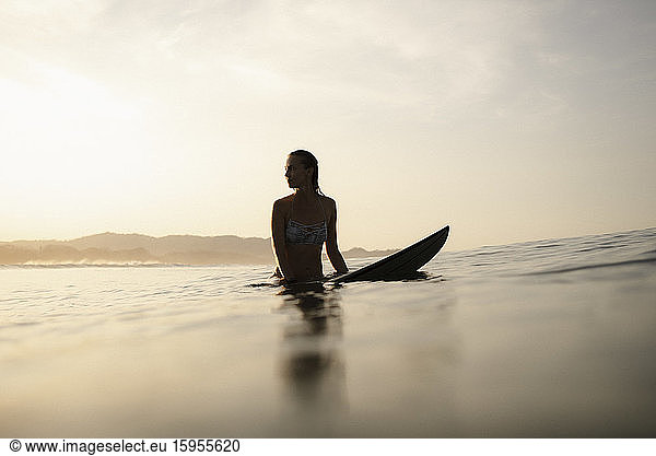 Weibliche Surferin sitzt abends auf dem Surfbrett  Costa Rica