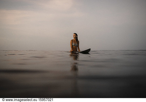 Weibliche Surferin sitzt abends auf dem Surfbrett  Costa Rica