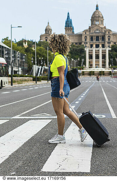 Weibliche Touristin beim Überqueren der Straße mit Koffer auf der Straße in der Stadt