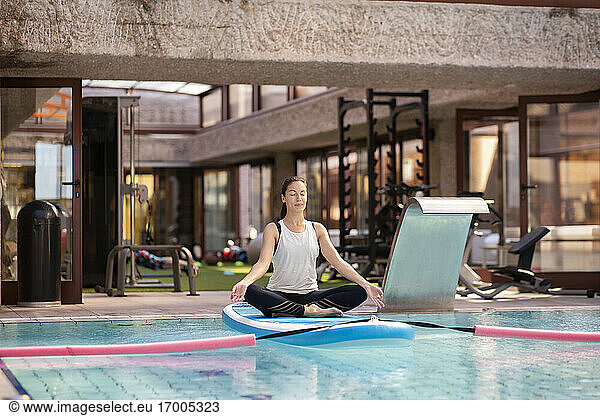 Weibliche Yogalehrerin im Lotussitz auf dem Paddleboard über dem Schwimmbad