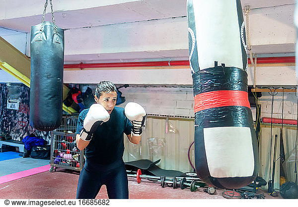 Weiblicher Boxer  der in einem Boxstudio auf einen riesigen Sandsack einschlägt.