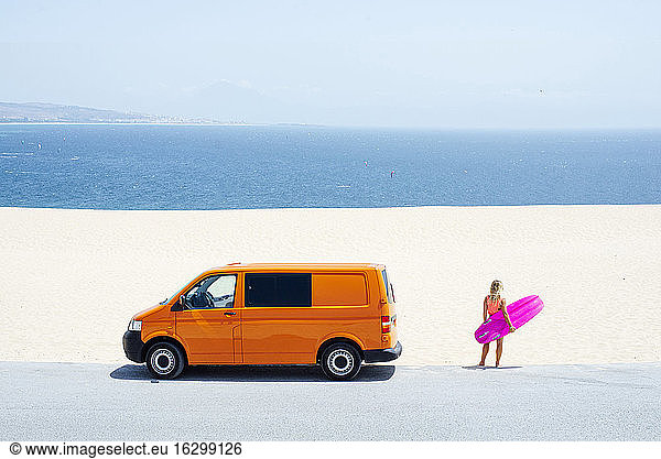 Weiblicher Reisender  der auf das Meer schaut  während er mit einem Surfbrett am Strand steht  an einem sonnigen Tag