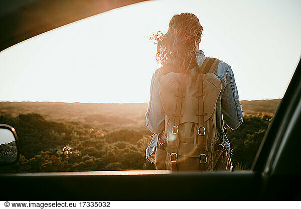 Weiblicher Rucksacktourist bei Sonnenuntergang aus dem Autofenster gesehen