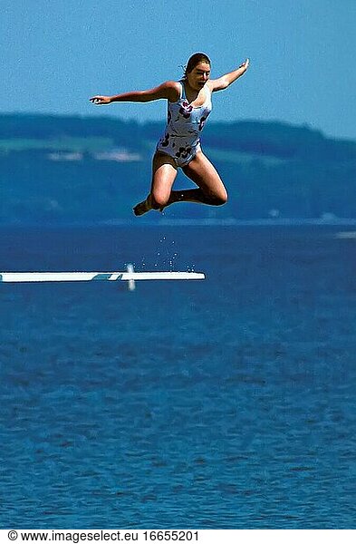 Weiblicher Teenager springt von einem Sprungbrett ins Wasser.