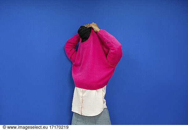 Weiblicher Unternehmer  der sein Sweatshirt auszieht  während er an einer blauen Wand am Arbeitsplatz steht