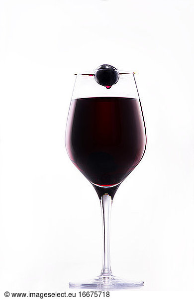 Wein tropft von einer roten Traube auf ein edles Glas Rotwein;
