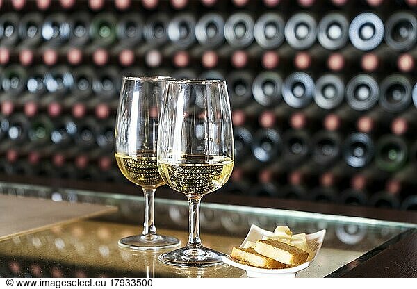 Weinprobe in der Weinkellerei  2 Gläser Weißwein mit Toast und Käse  dahinter Hunderte von Weinflaschen gestapelt  Lanzarote  Spanien  Europa