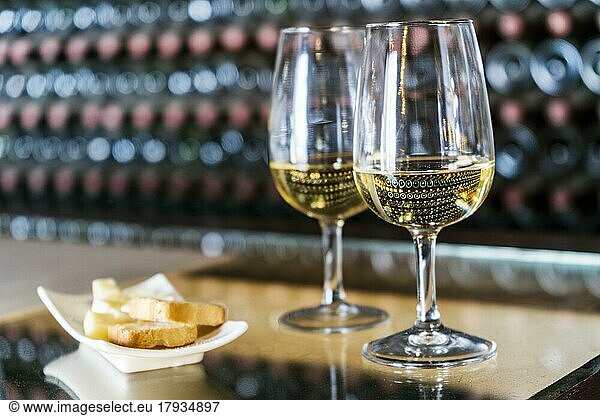 Weinprobe in der Weinkellerei  2 Gläser Weißwein mit Toast und Käse  dahinter Hunderte von Weinflaschen gestapelt  Lanzarote  Spanien  Europa
