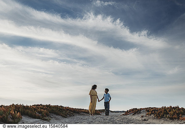 Weite Ansicht von Mutter und Sohn am Strand vor wolkenblauem Himmel