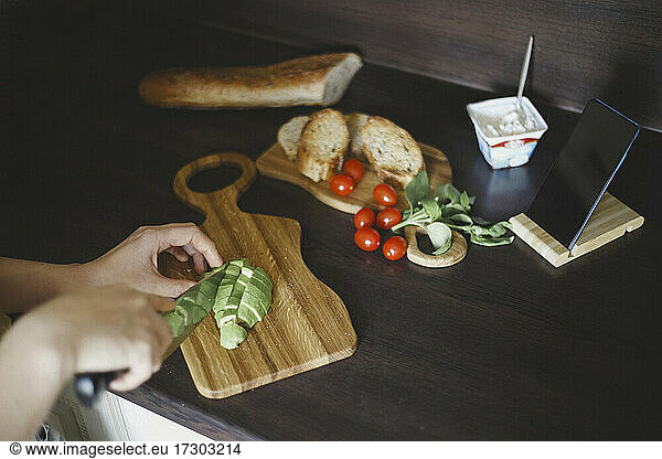 Weitwinkel von Brot  Tomaten  Smartphone und Händen  die den Avocado schneiden