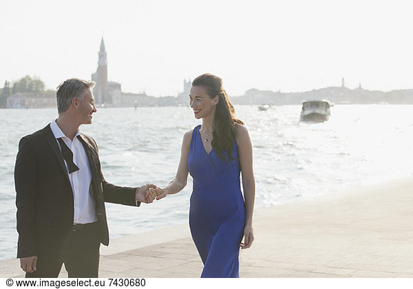 Well-dressed couple holding hands at waterfront in Venice