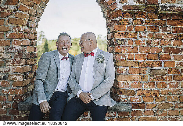 Well dressed happy gay couple sitting on window during wedding