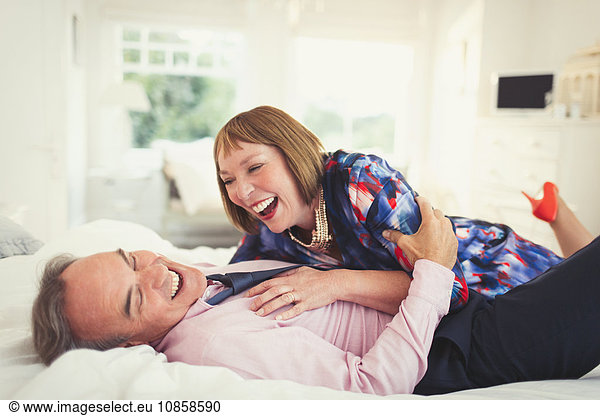 Well-dressed mature couple laughing on bed