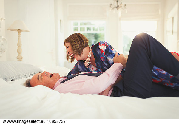 Well-dressed mature couple laughing on bed