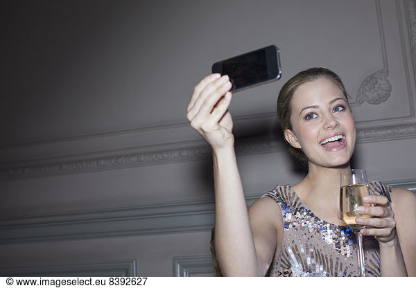 Well dressed woman with champagne taking self-portrait with camera phone