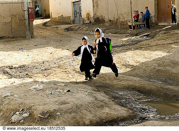 While on her way to school with a friend  one girl leaps over a mud patch in Kabul.