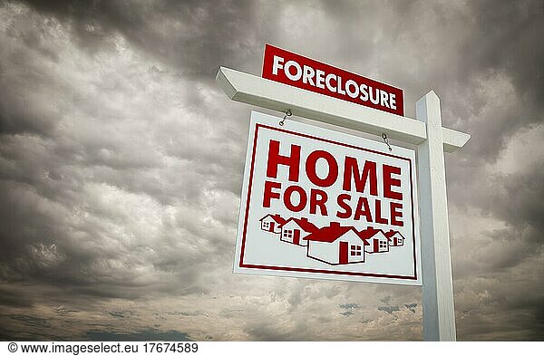 White and red foreclosure home for sale real estate sign over ominous cloudy sky