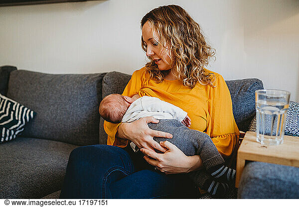 White blonde mum breastfeeding newborn baby boy on couch at home