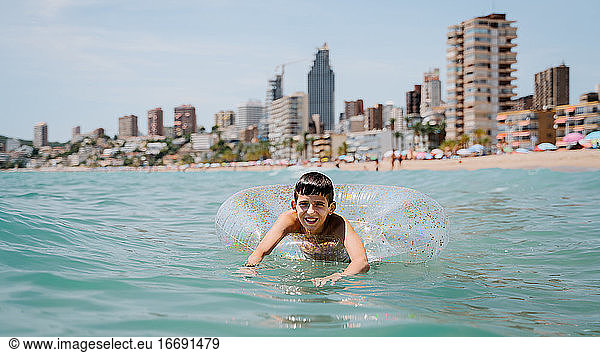 white boy swimming in a float in the sea with buildings on background