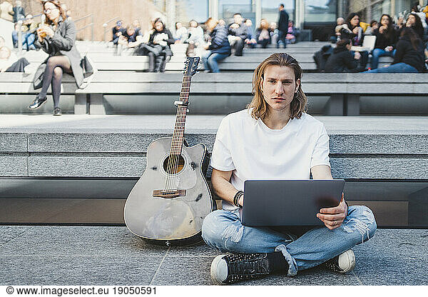 white man using laptop device outdoor next to his acoustic guitar