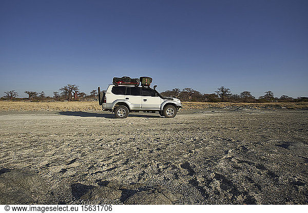 White off-road vehicle with baobab trees in background against clear sky  Makgadikgadi Pans  Botswana