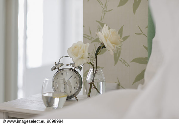 White roses  alarm clock and water glass on bedside table