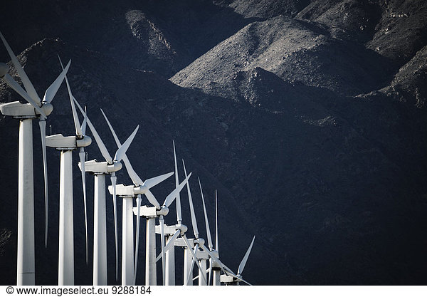 White wind turbines  in a row  against the backdrop of a snow capped mountain.