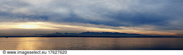 Wide angle view of Puget Sound with Olympic mountain range beyond and cloudy sky.