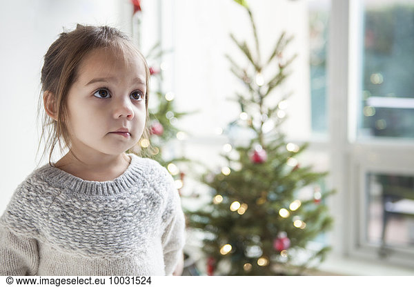 Wide-eyed girl looking up in front of Christmas tree