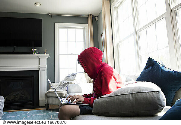 Wide Side View of Tween Boy in Hooded Sweatshirt Working on Laptop