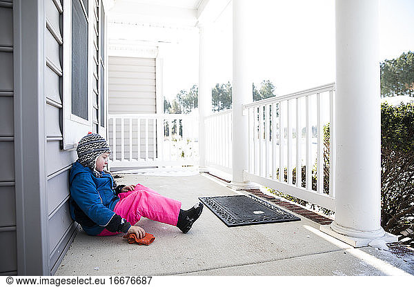 Wide View of Boy in Pink Snow Pants Sitting on Snowy Front Porch