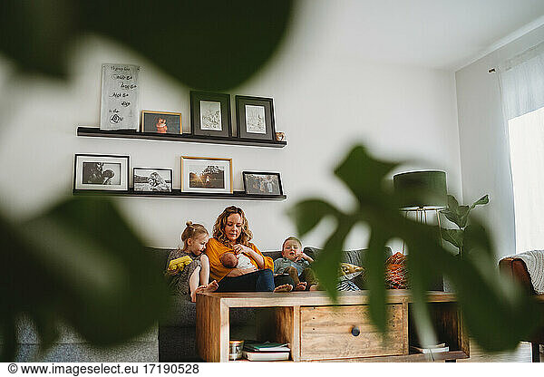 Wide view of cozy living room with plants of mom and children on sofa