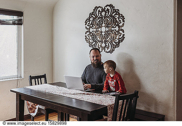 Wide view of father trying to work from home with toddler standing