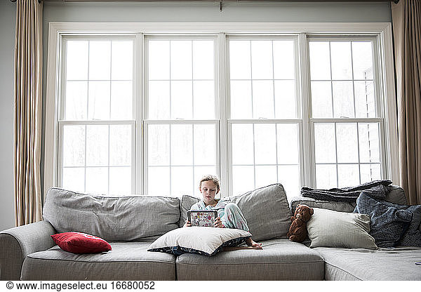 Wide View of Girl Home Sick From School On Couch With Tablet and Teddy