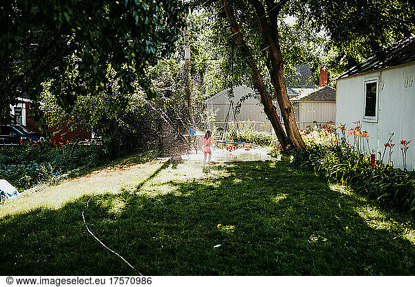 Wide view of girl running through sprinkler in backyard