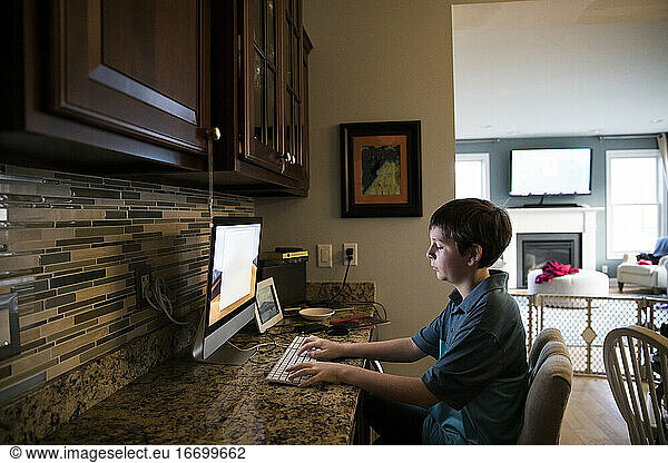 Wide View of Tween Boy Typing on Keyboard at Computer Desk