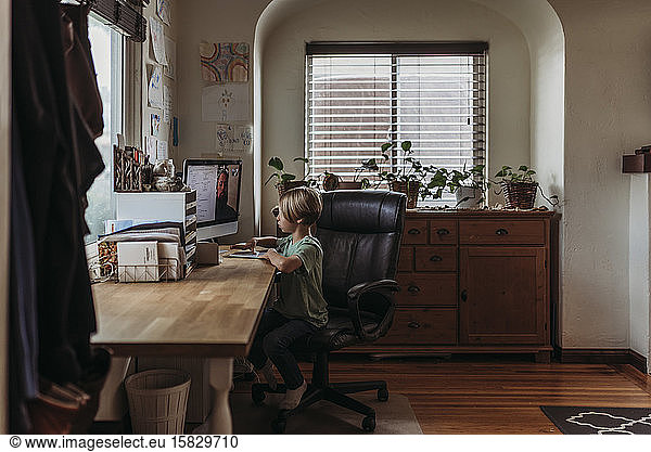 Wide view of young boy taking online class during isolation