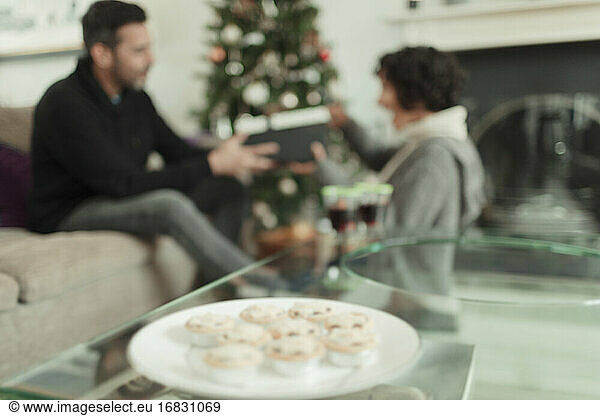Wife opening Christmas gift from husband behind tray of mince pies