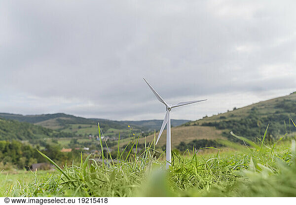 Wind turbine model on grass under cloudy sky in meadow