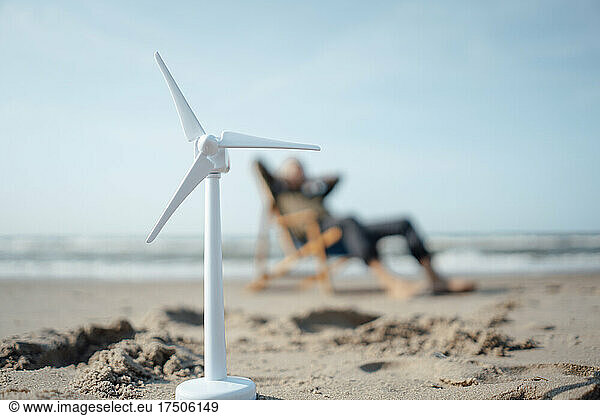 Wind turbine model on sand with senior man in background