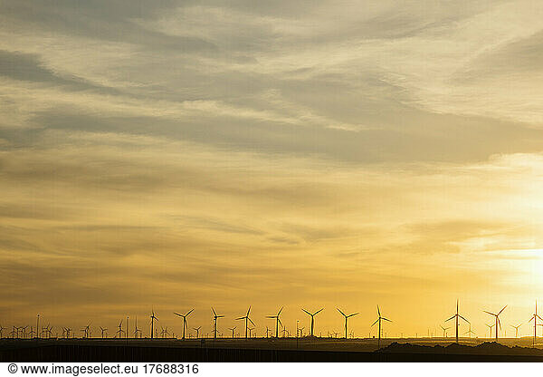 Wind turbines under yellow sky at sunset