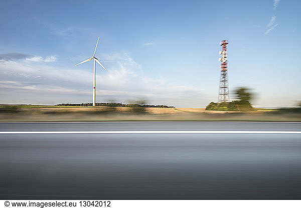 Windmill and communications tower against sky seen through car window