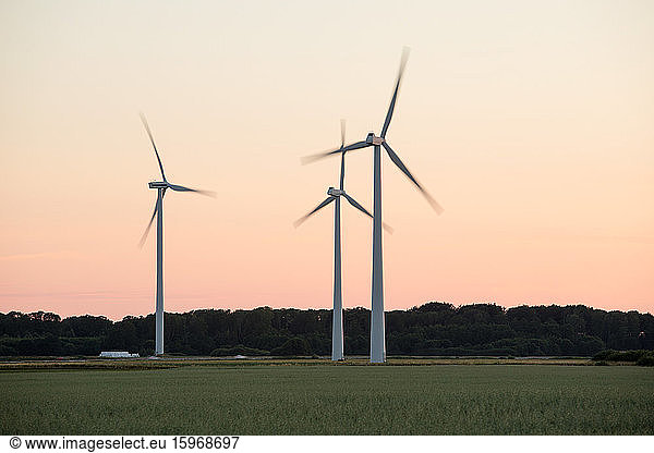 Windmills in motion on grassy field against clear sky during sunset
