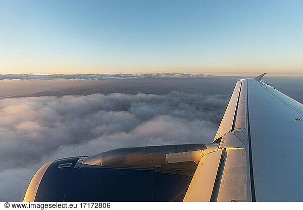 Wing of airplane flying over clouds at dawn